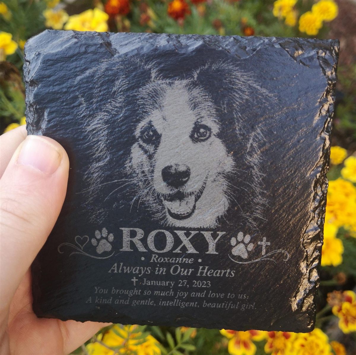 A dog portrait engraved on slate that reads Roxy, Always in Our Hearts, held in a hand